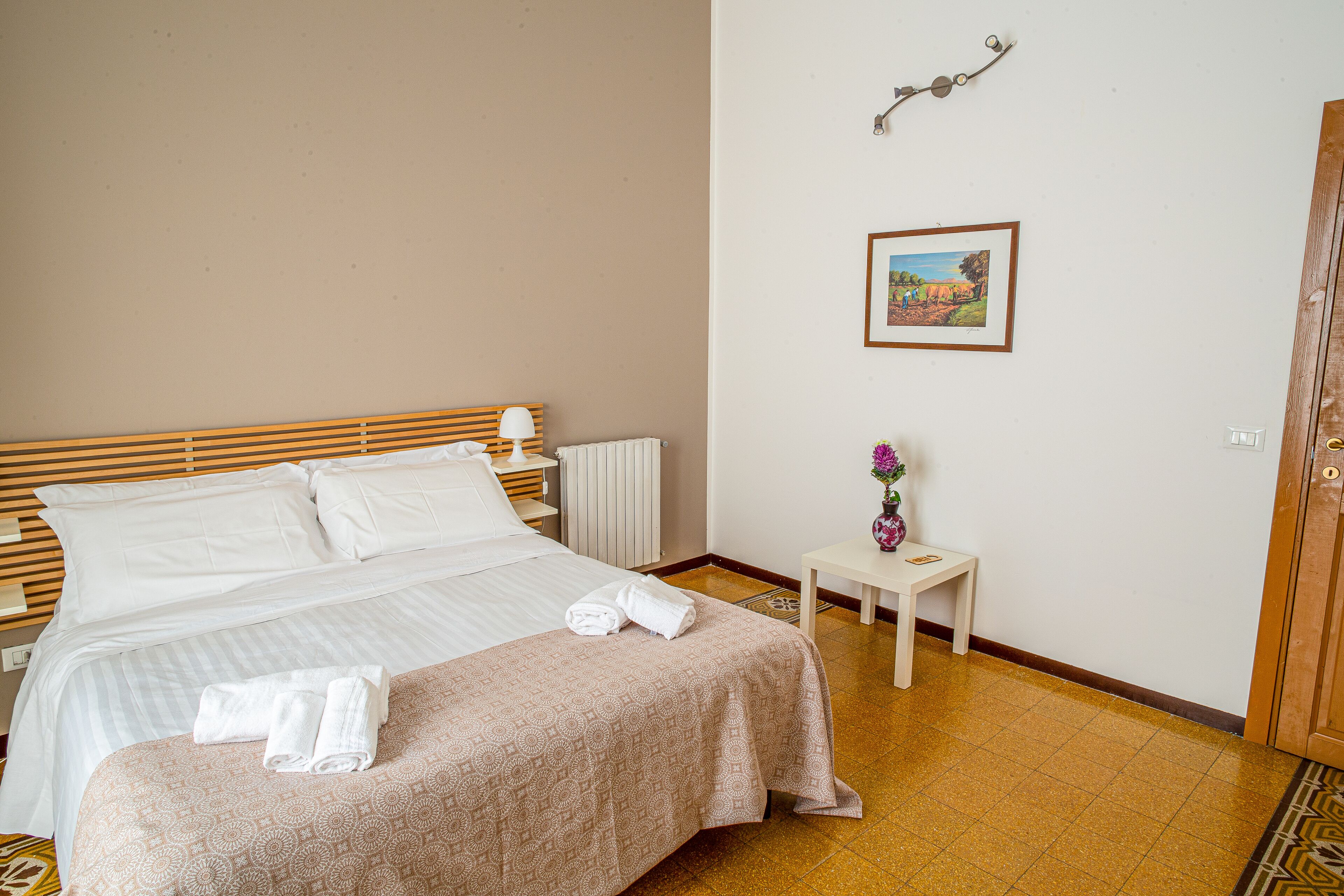 A neatly made bed with a patterned bedspread, a bedside table with a lamp, and a framed picture on the wall.