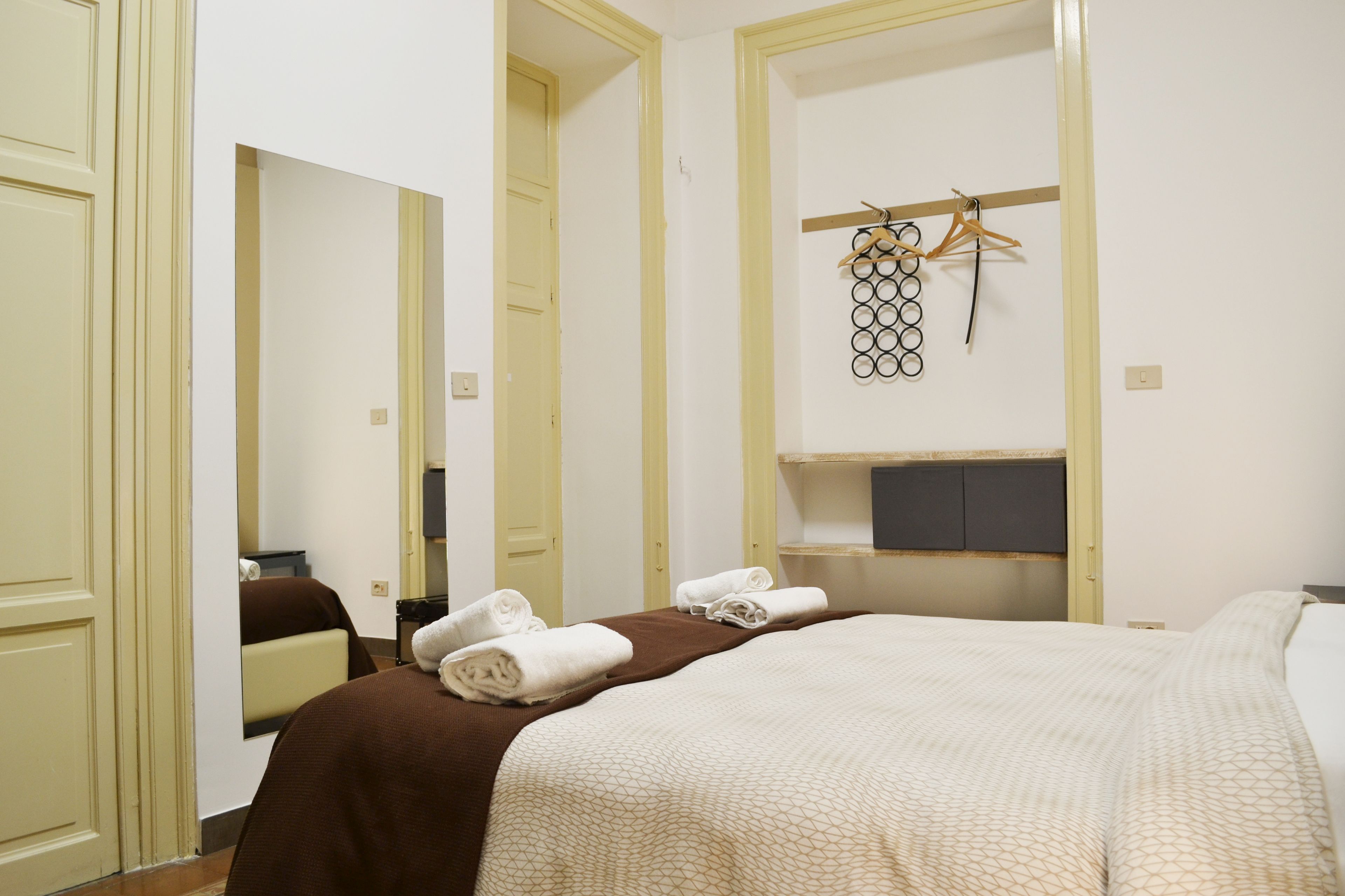 A hotel room with a bed, a mirror, a wardrobe, and a towel rack.