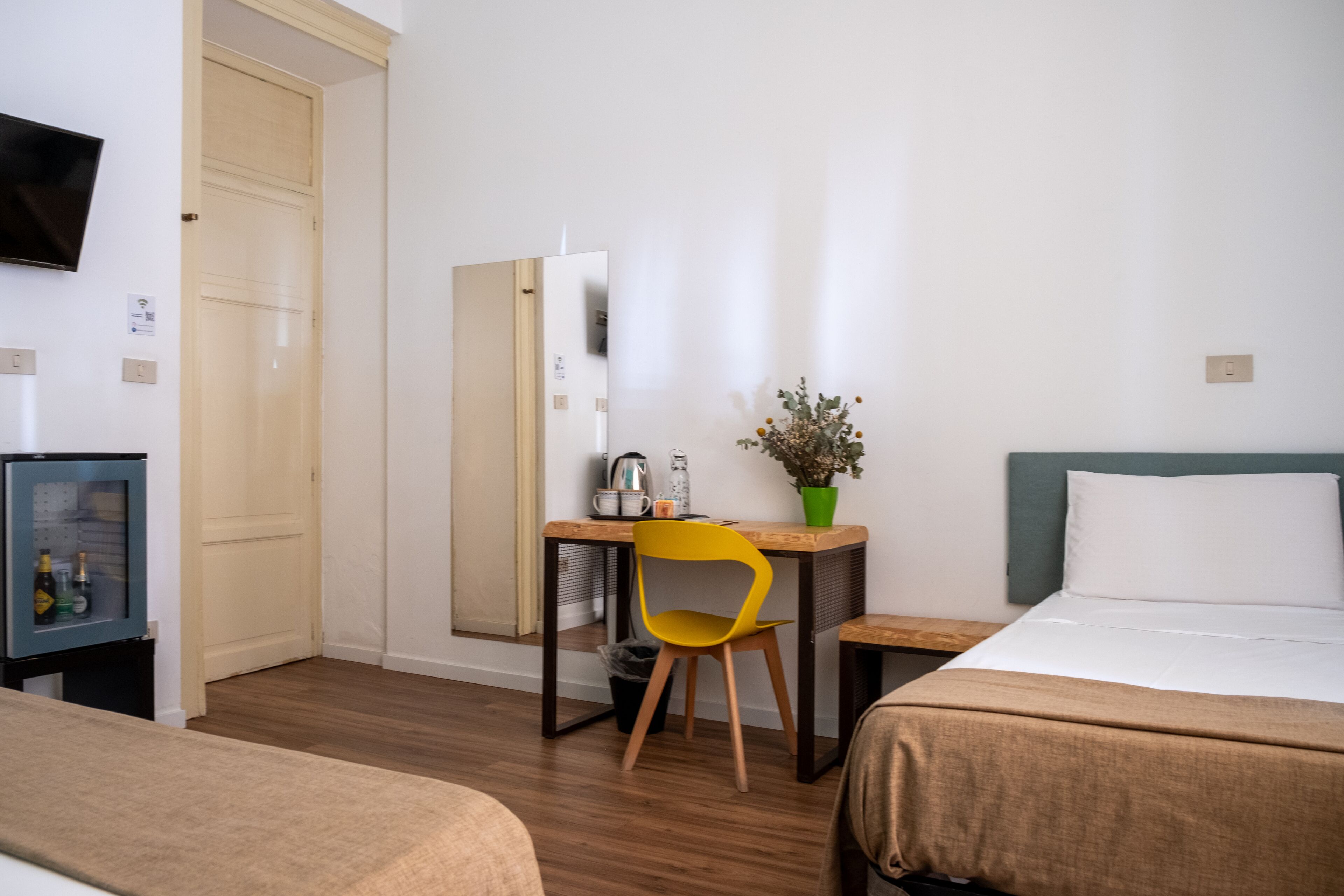 A hotel room with two beds, a desk with a chair, a TV, and a small table with a plant.