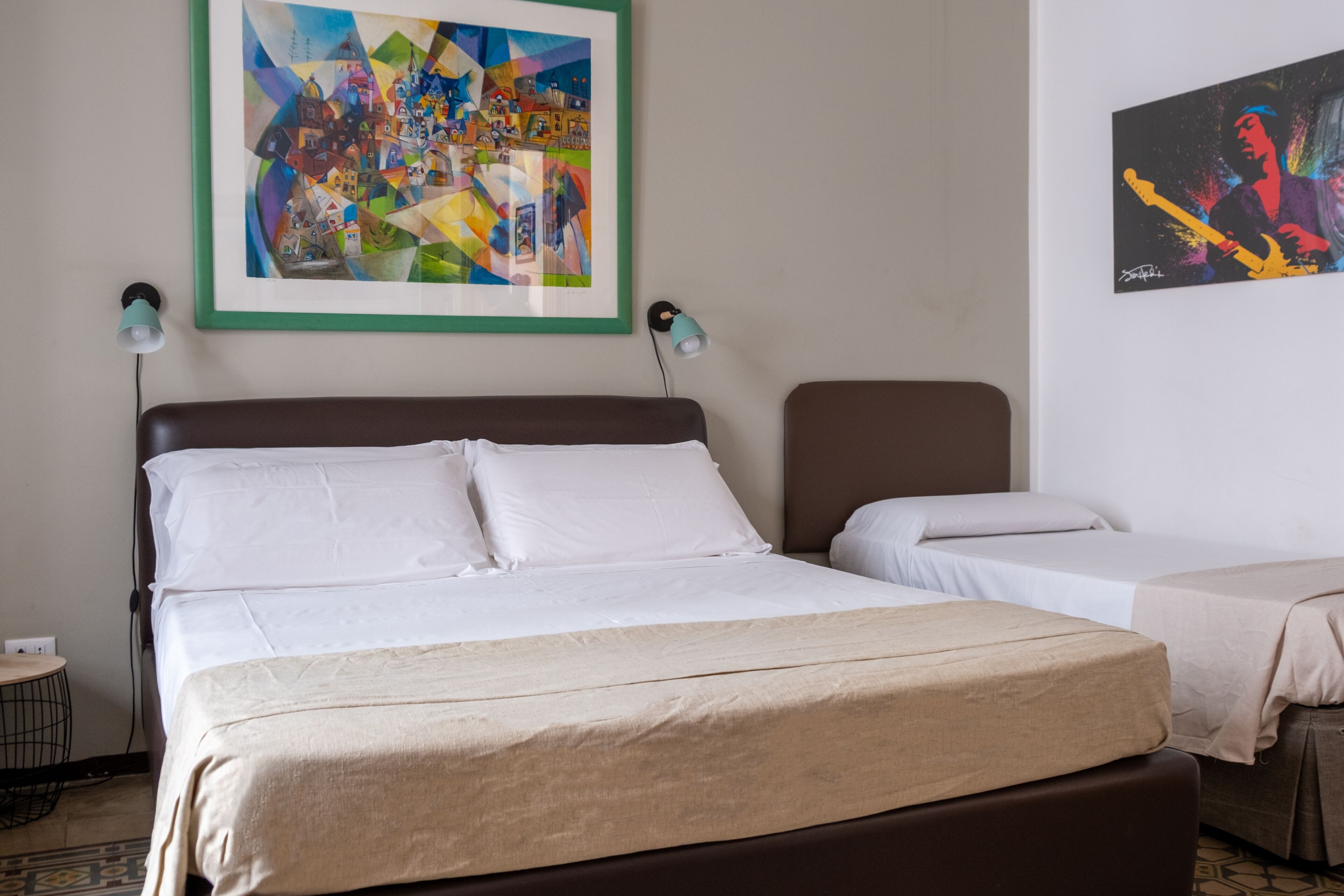 A hotel room with a large bed, two bedside tables, and two lamps. There are two paintings on the wall.