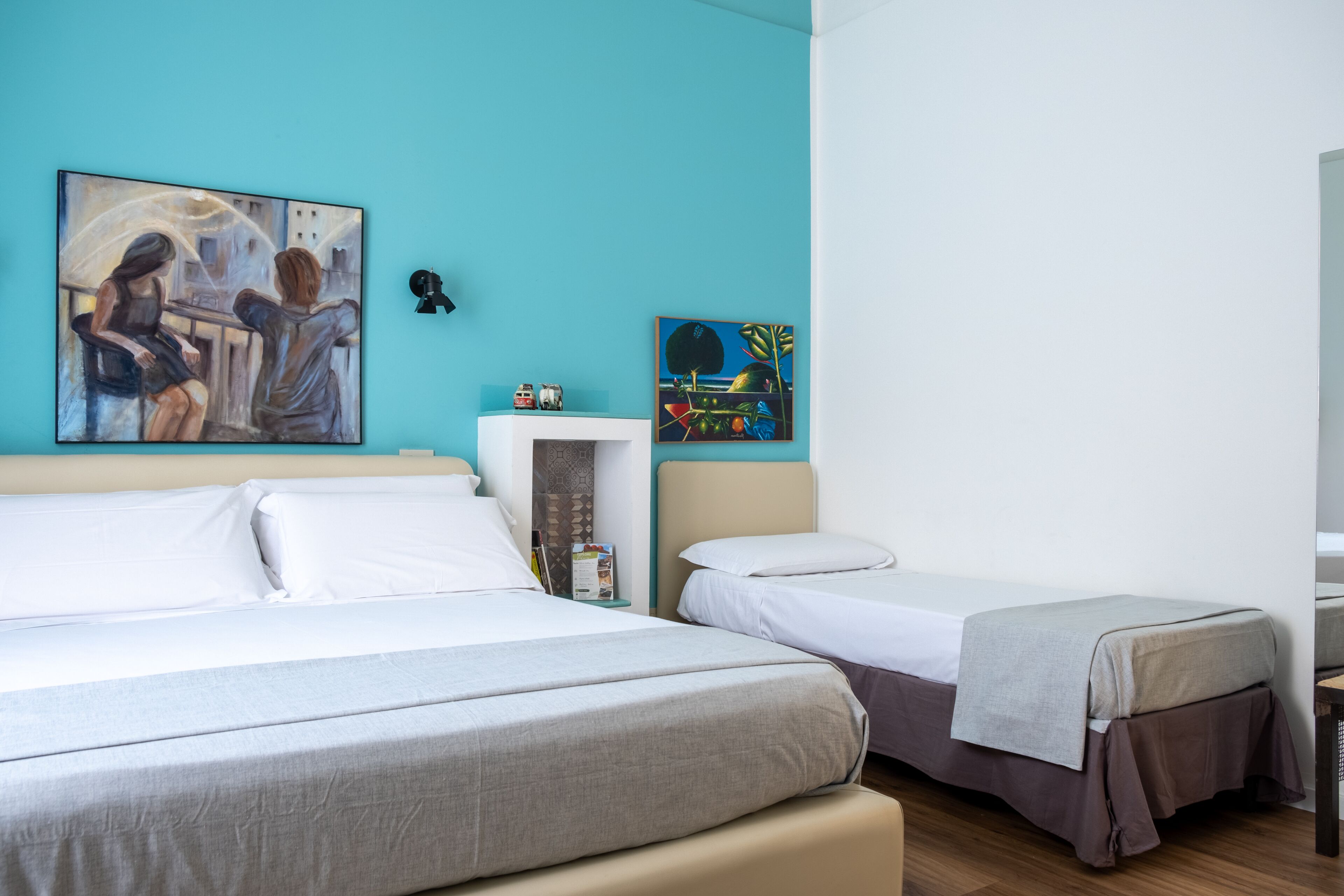 Habitació d'hotel amb dos llits, una paret d'accent color turquesa i dues pintures.