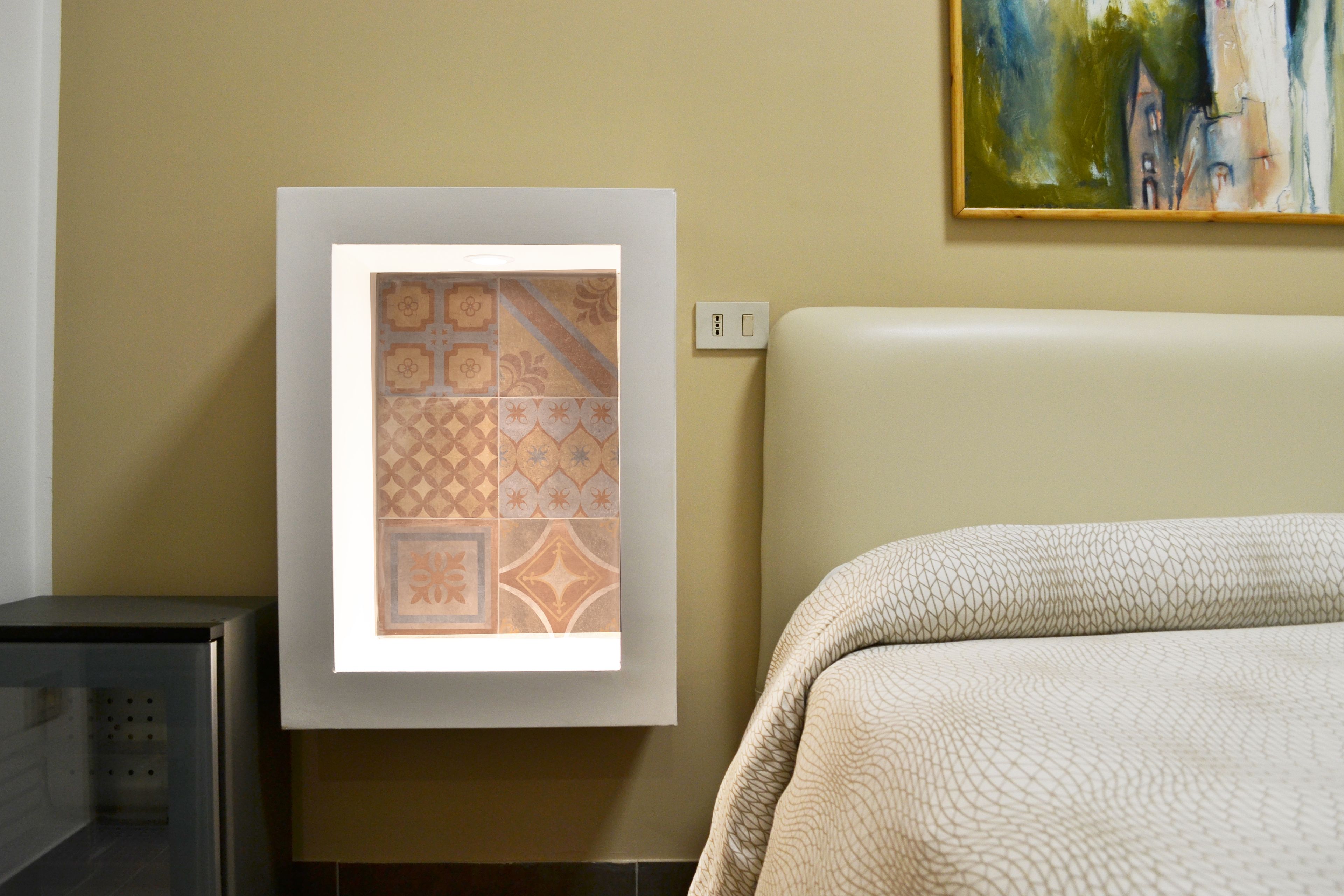 Un cuadro con azulejos en una pared, un enchufe y una cama con una manta texturizada.