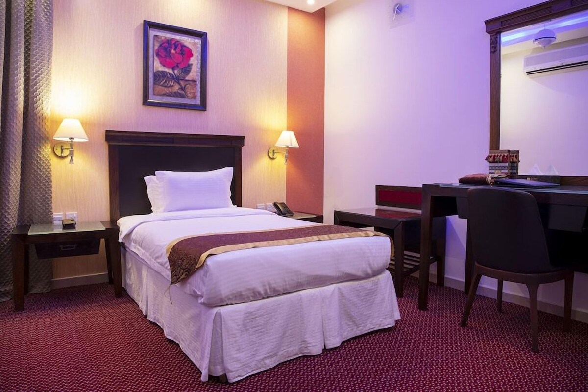 A hotel room with a bed, two bedside lamps, a desk with a chair, and a mirror.