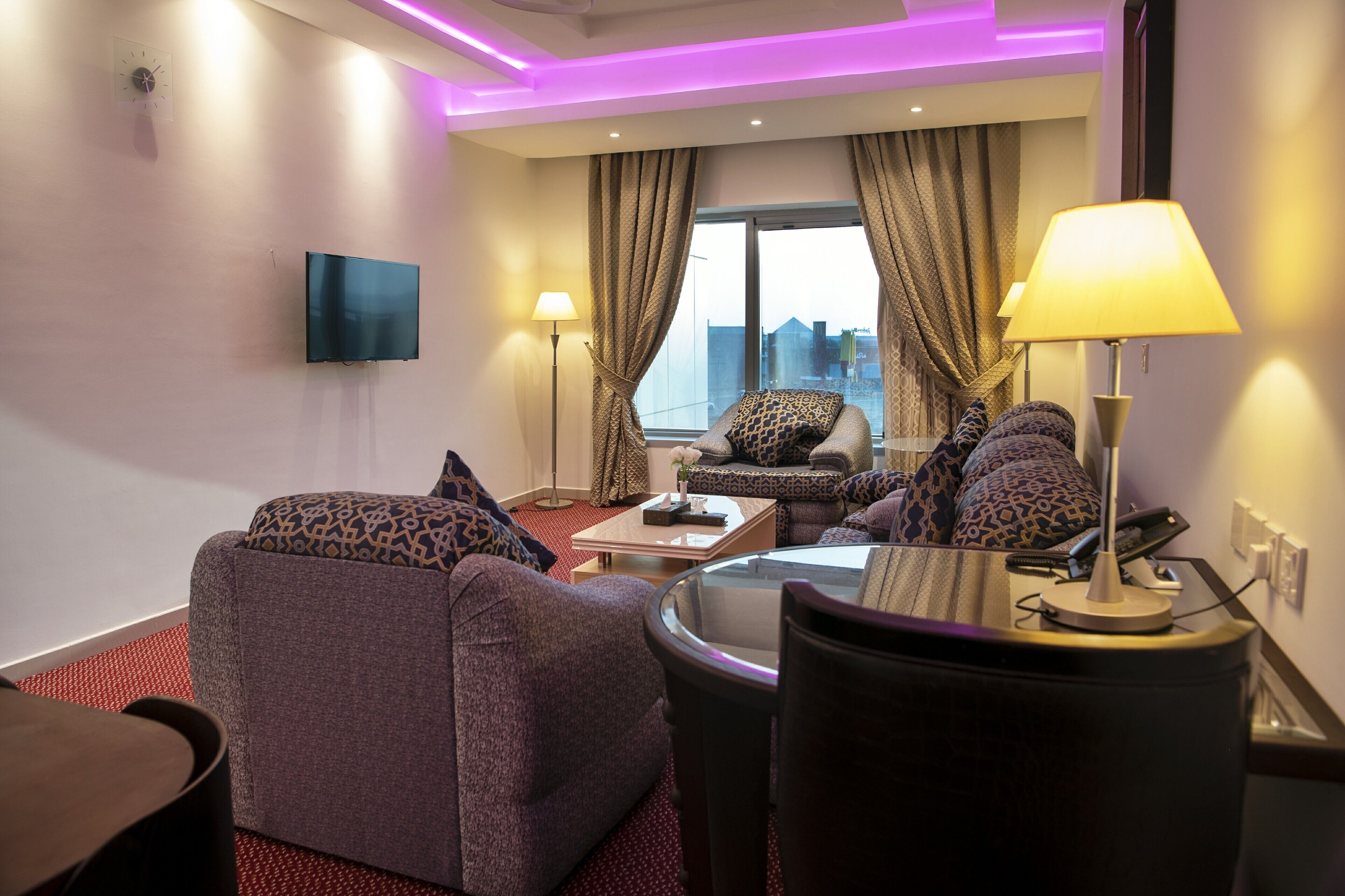 Una habitación de hotel moderna con un conjunto de sofá, una mesa de centro, un televisor montado en la pared y vistas a la ciudad a través del ventanal.