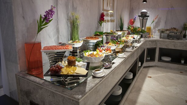 A buffet with various food items and a vase with purple flowers. - Jazan Inn (Jizan)