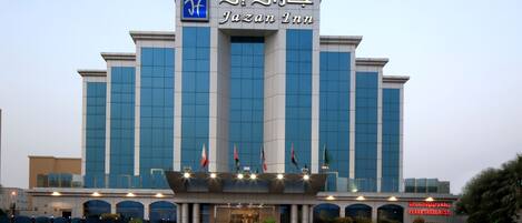 A modern building with a prominent sign reading "Jazan Inn" and multiple flags.