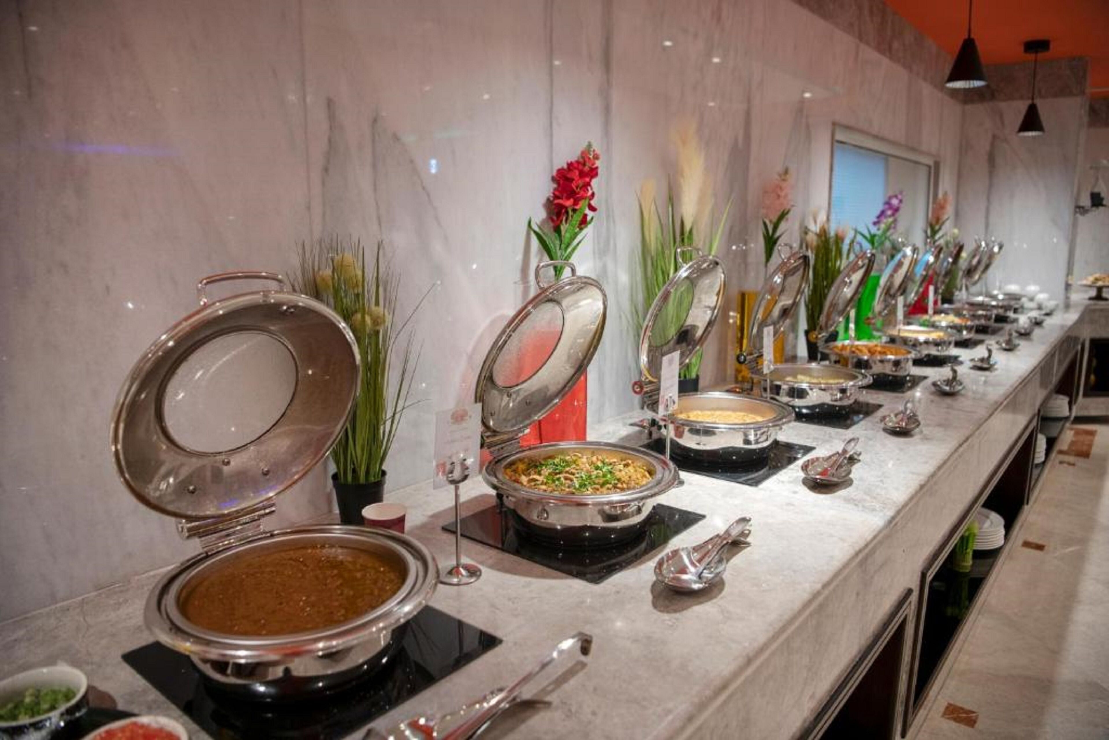 A buffet setup with various food stations, each with a covered serving dish and a spoon.