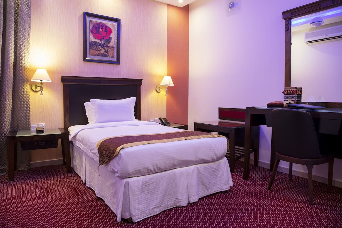 A hotel room with a bed, two bedside lamps, a desk with a chair, and a mirror.