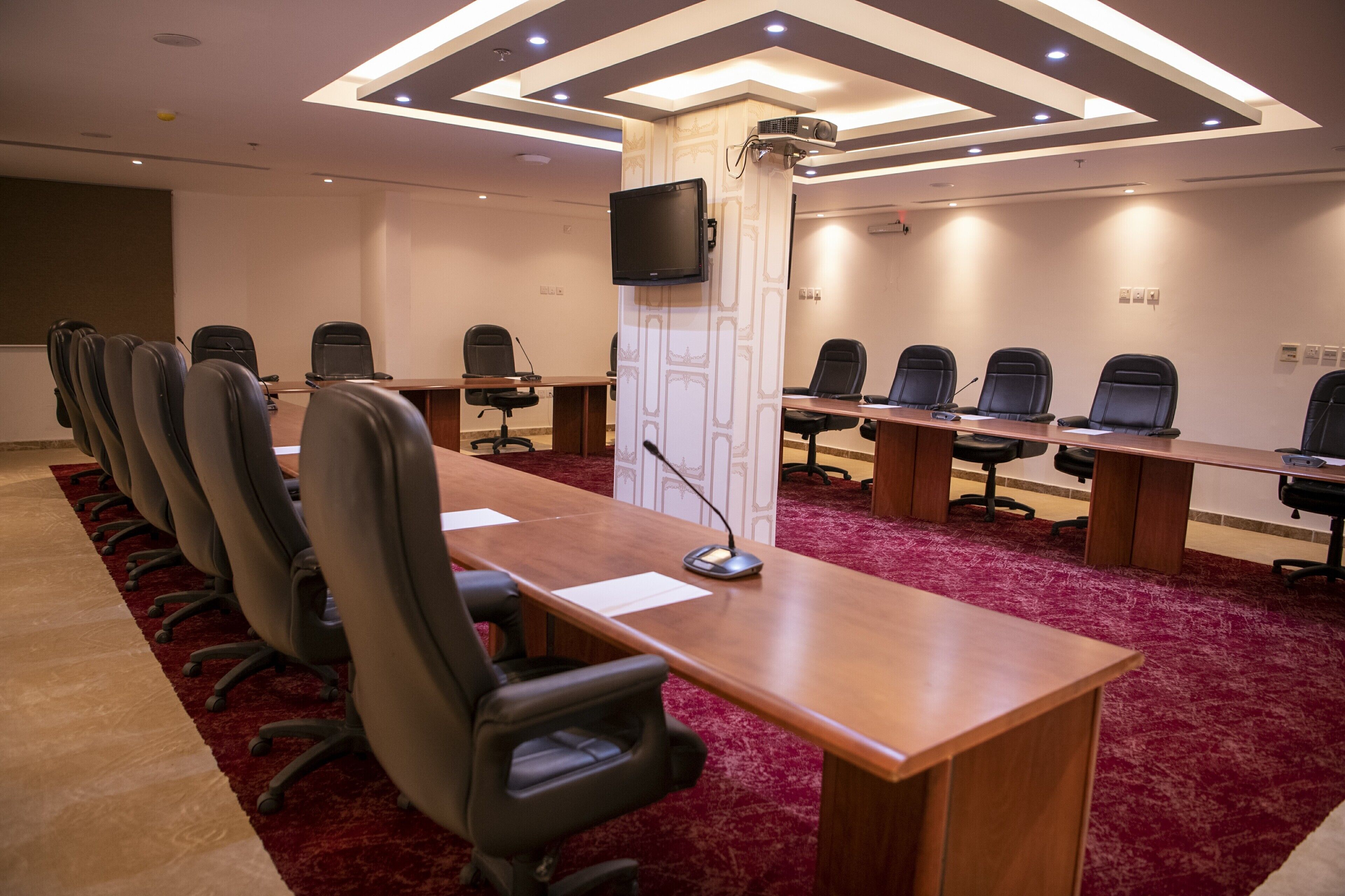 Un salón de conferencias con una larga mesa, varias sillas, un proyector y una televisión.