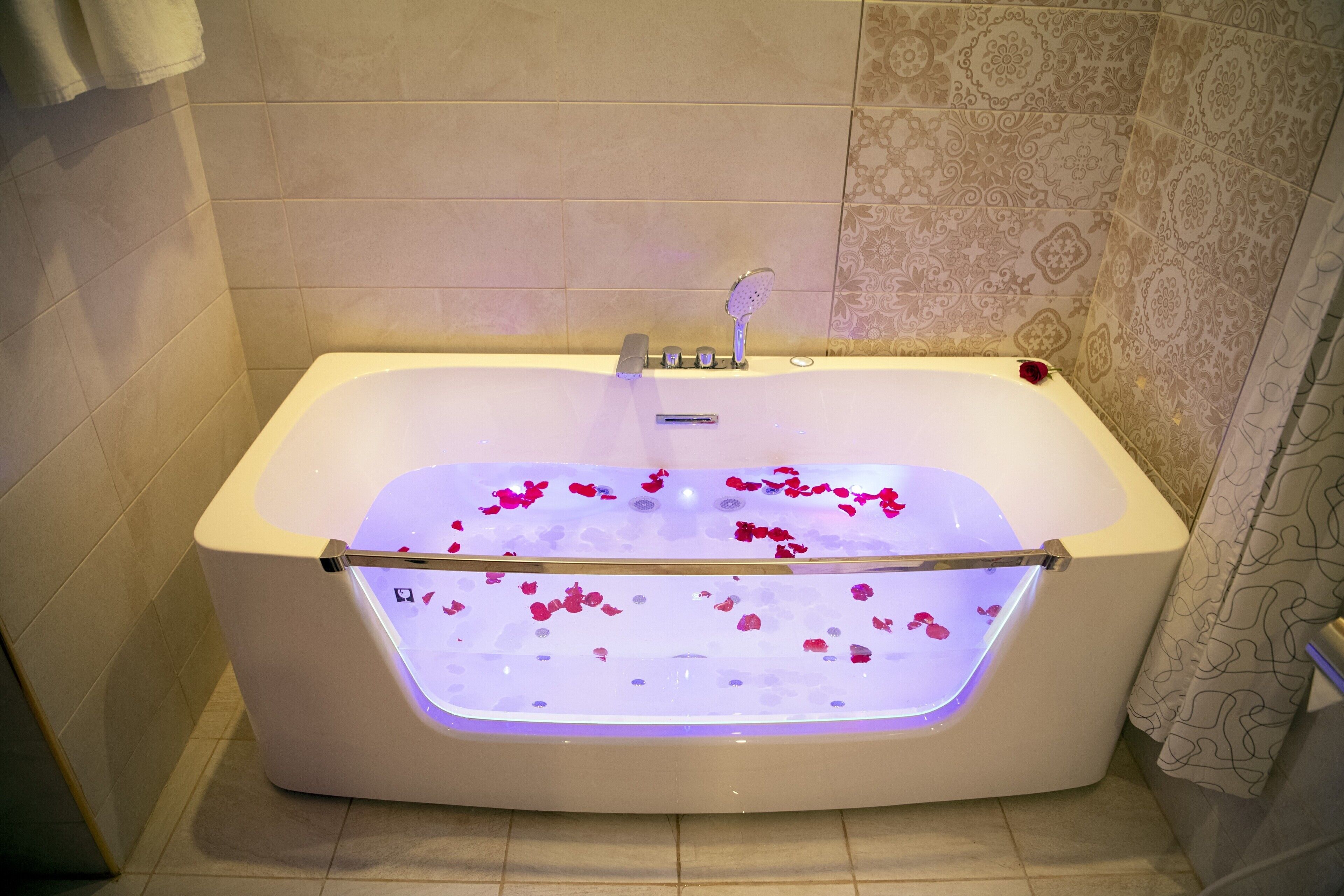 A modern bathroom with a bathtub filled with rose petals and illuminated from below.