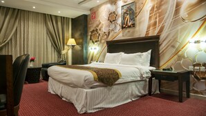 A hotel room with a large bed, a desk, a chair, and a lamp. - Jazan Inn (Jizan)