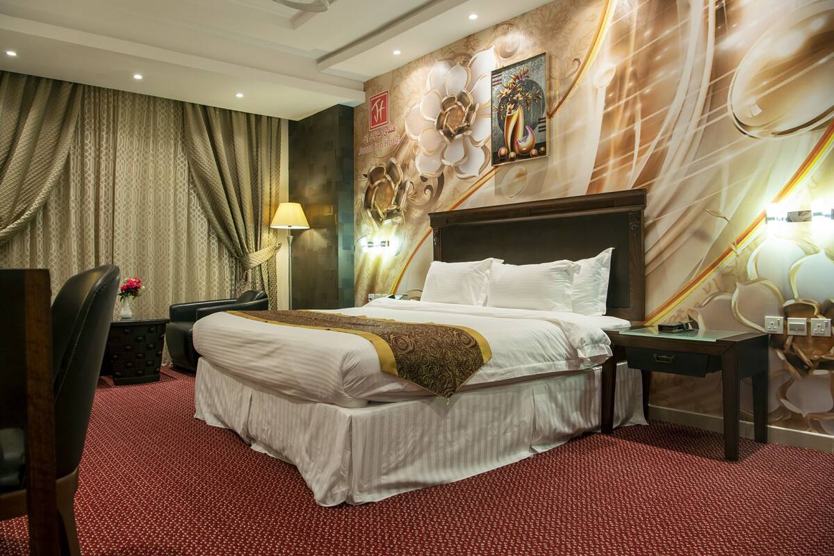 A hotel room with a large bed, a desk, a chair, and a lamp.