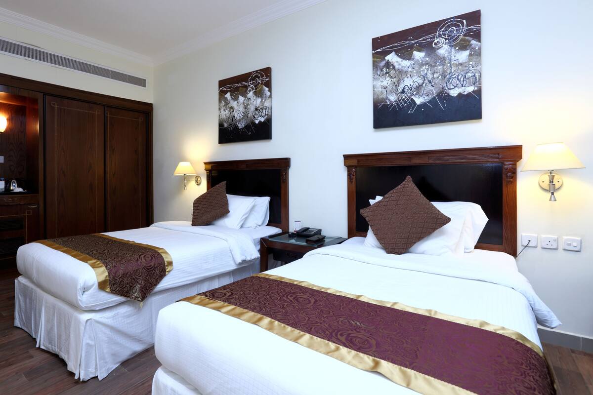 A hotel room with two beds, wooden headboards, bedside lamps, and artwork on the walls.