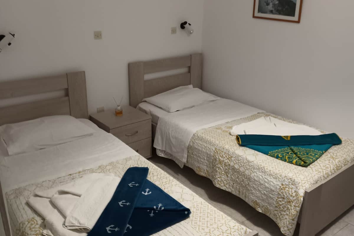A room with two single beds, a nightstand, a bedside table, and a wall-mounted lamp.