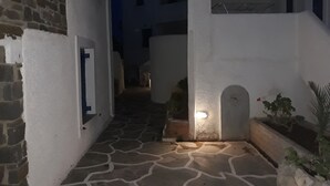 A narrow stone-paved courtyard with white walls, a small illuminated window, and a potted plant. - Holidays in Paros (Paros)