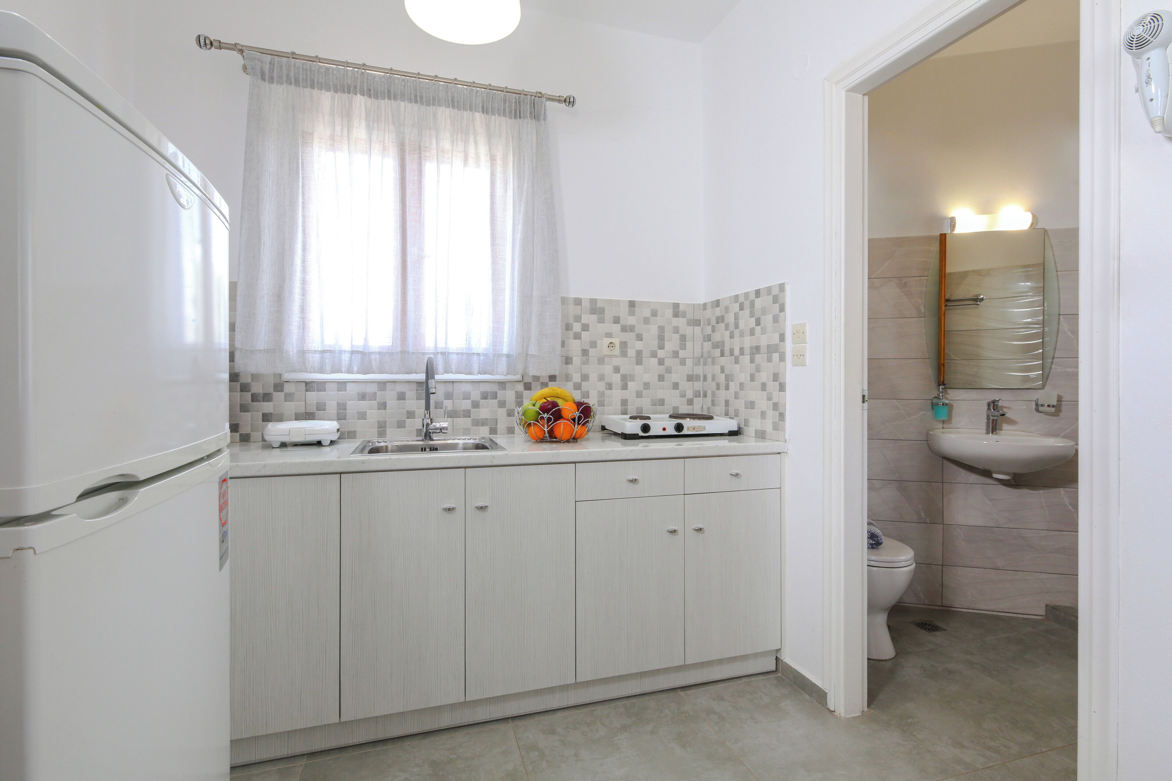 Una cocina compacta con refrigerador, pileta y un frutero en la encimera.