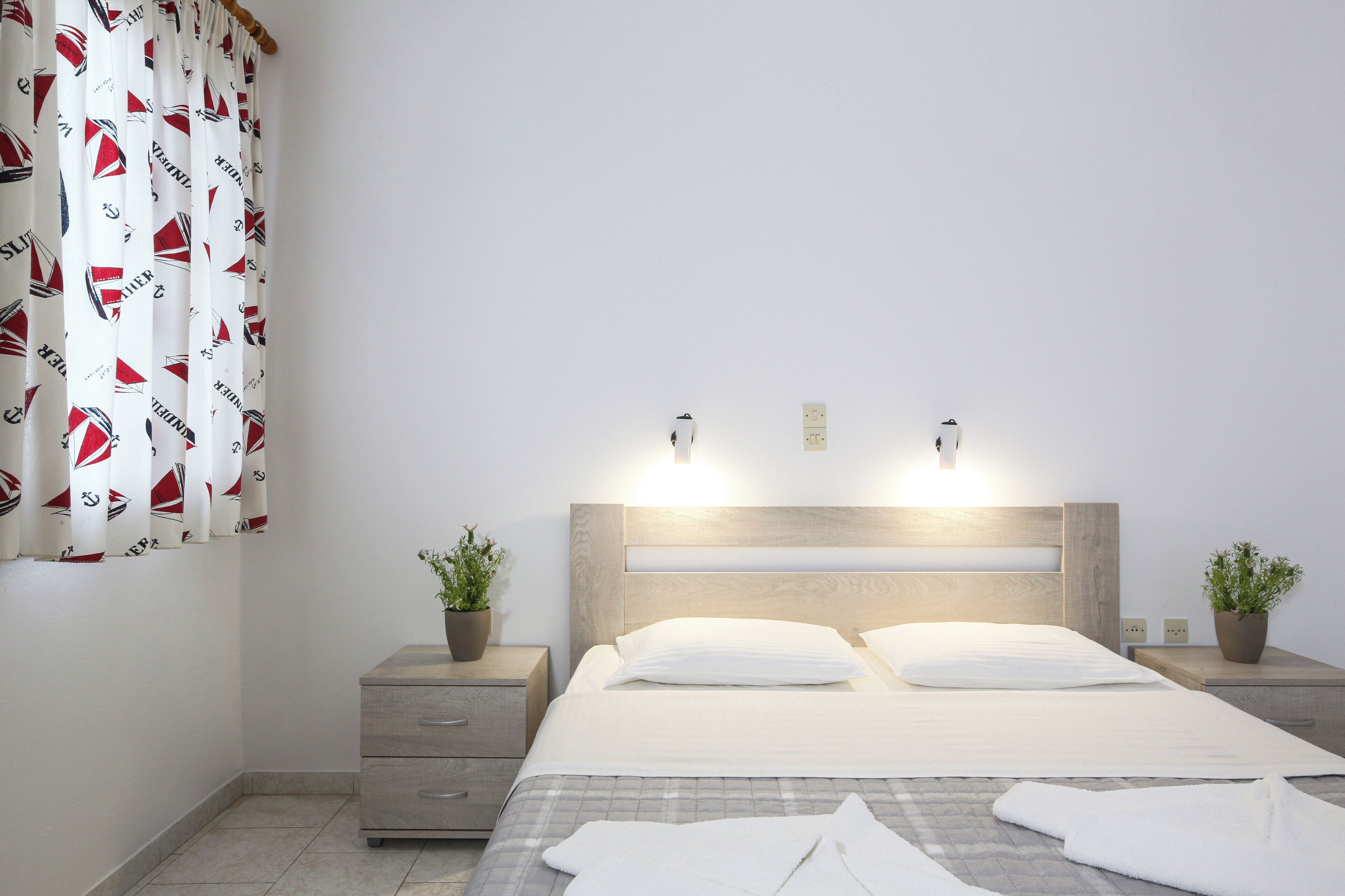 Un lit bien fait, avec du linge de lit blanc, une tête de lit en bois et des tables de chevet ornées de plantes en pot.