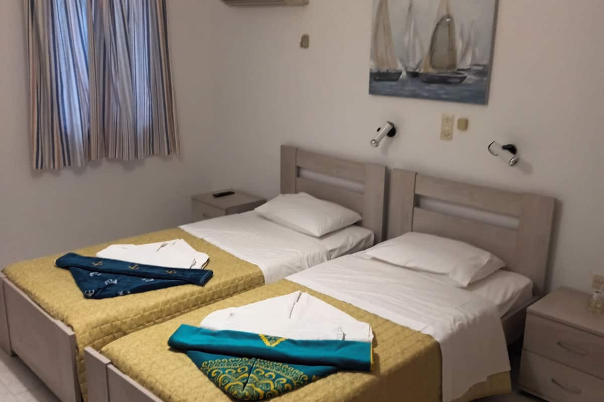 A hotel room with two beds, a painting of a sailboat, an air conditioning unit, and a hanging light fixture.