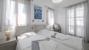 A hotel room with two beds, a painting on the wall, and a chair. - Holidays in Paros (Paros)