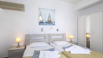 A hotel room with two beds, a painting of sailboats, bedside lamps, a wardrobe, and a heater.