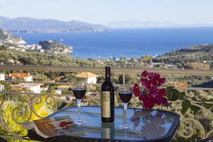 Una mesa con una botella de vino y dos copas en un balcón con vistas al paisaje costero.
