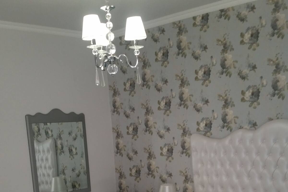 A neatly arranged bedroom with a large bed, a bedside table, a mirror, and a chandelier.