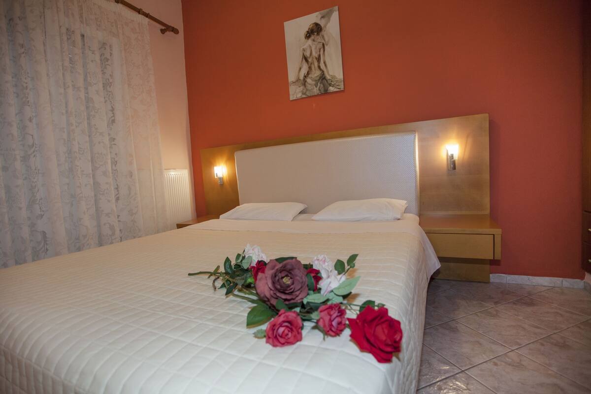 A neatly made bed with a floral arrangement, a painting on the wall, and a nightstand with a lamp.