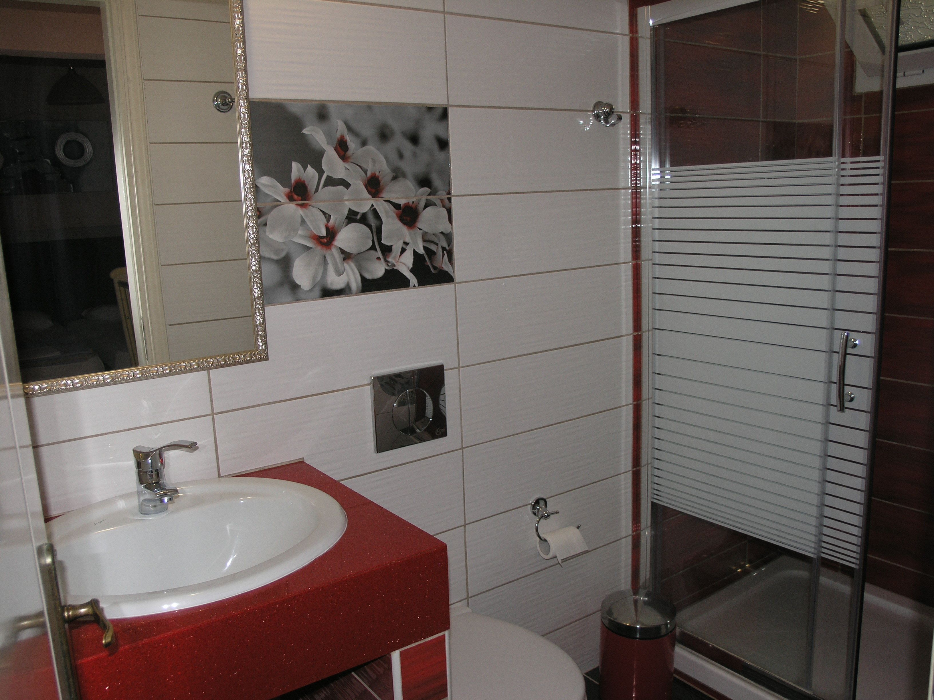 Une salle de bain avec un lavabo blanc, un plan de toilette rouge et un miroir orné d’un motif floral.