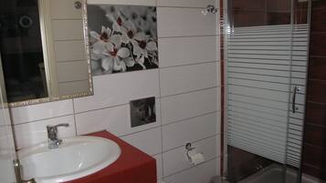 Une salle de bain avec un lavabo blanc, un plan de toilette rouge et un miroir orné d’un motif floral.