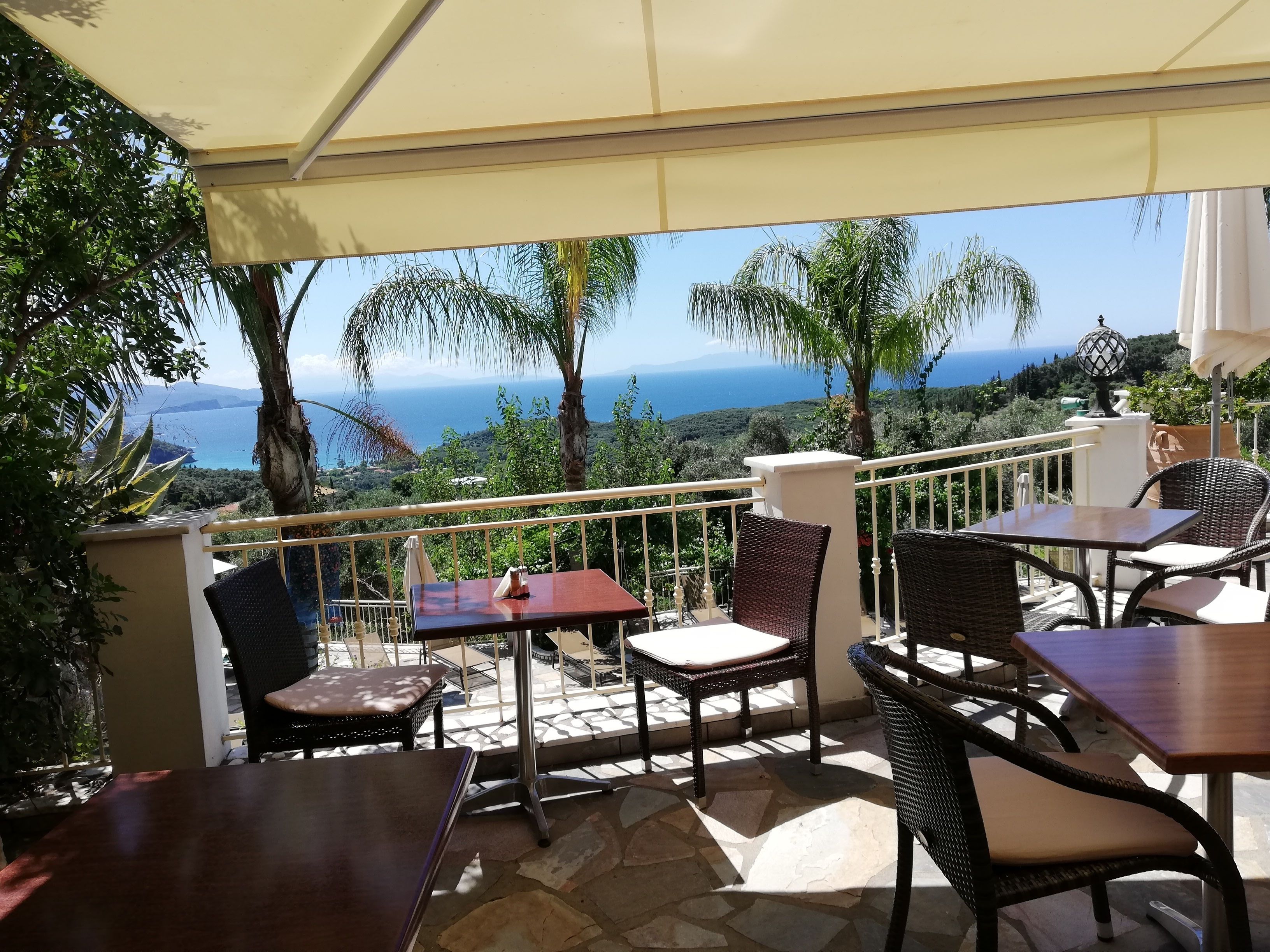 Una terraza con mesas y sillas, con vistas panorámicas al mar y las colinas.