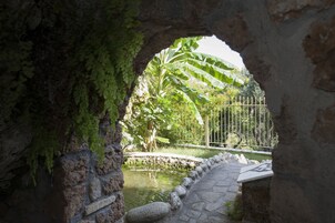 Un arco de entrada a un jardín con un estanque, un sendero de piedra y una valla de metal.