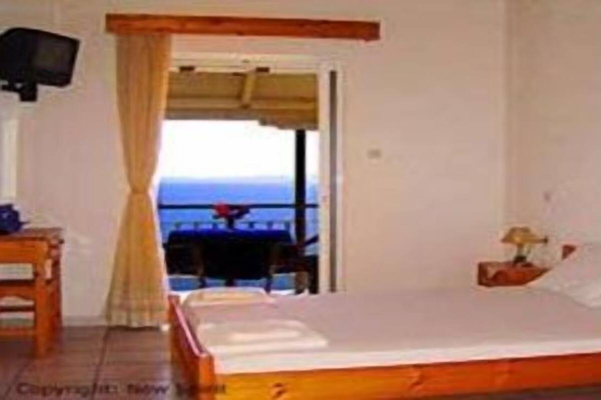 A bedroom with a bed, a nightstand, a TV, and a view of the sea.