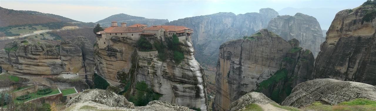 Un monastero arroccato su una scogliera rocciosa con vista panoramica sul paesaggio circostante.