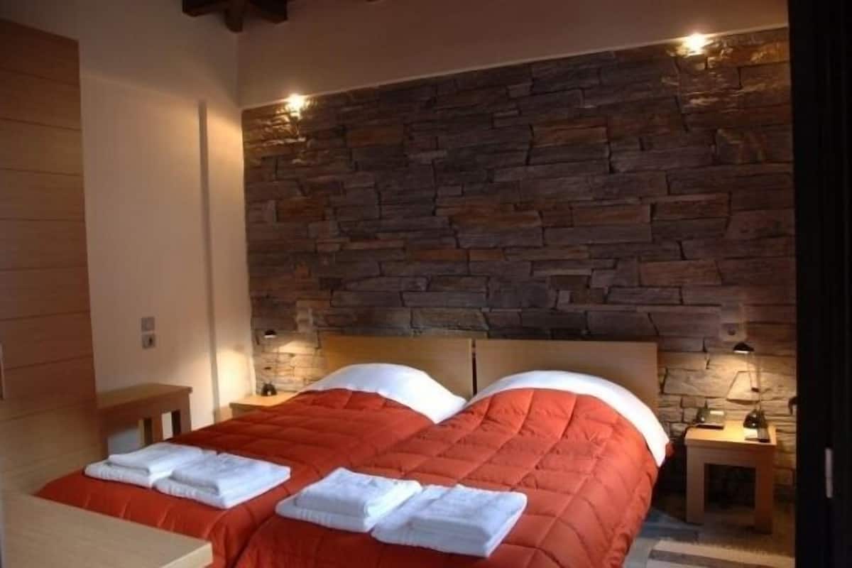 Een slaapkamer met een stenen muur, een bed met oranje beddengoed en twee nachtkastjes met lampen.