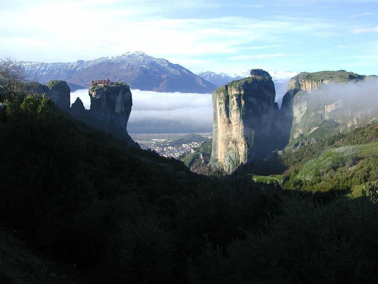 Un paysage montagneux caractérisé par d’imposantes formations rocheuses et offrant une vue lointaine sur une ville.