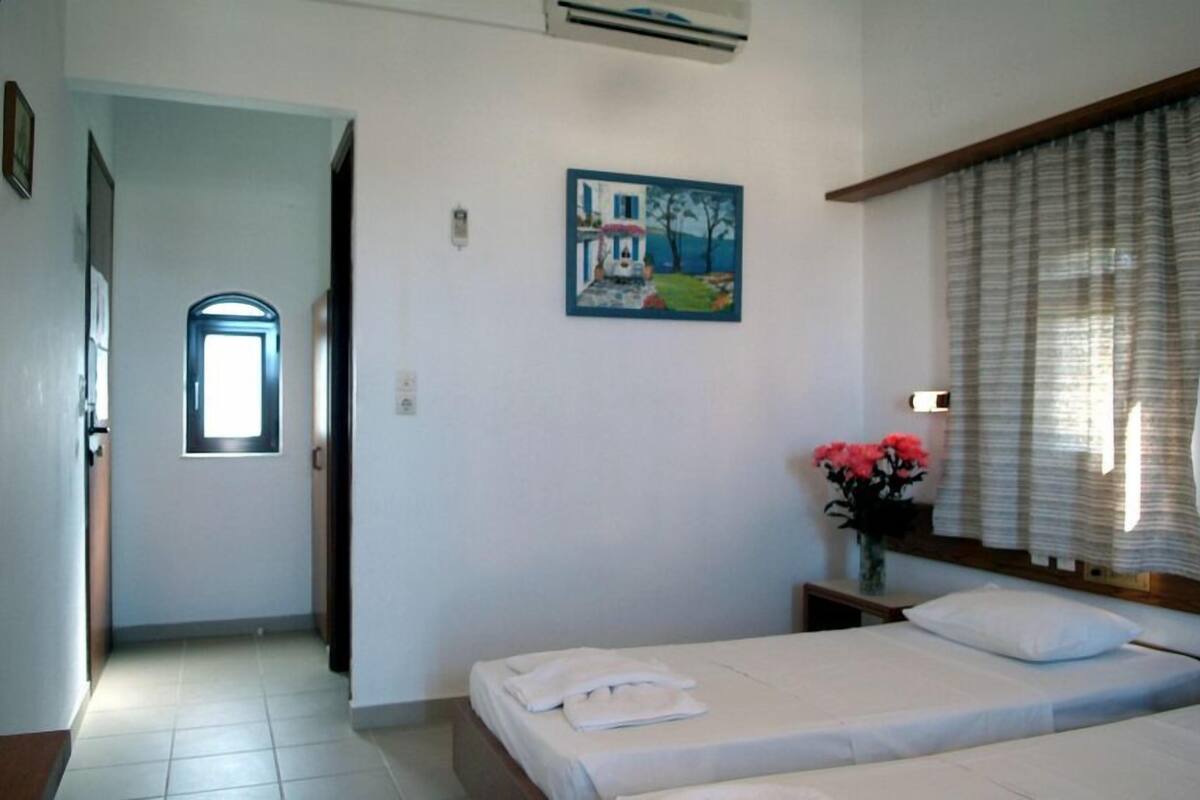 A bedroom with a bed, a painting, a window with curtains, and a vase with flowers.