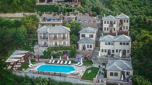 A large, multi-story hotel with a central swimming pool surrounded by lounge chairs and a flag. - Agapitos Villas & Guesthouses (Zagora-Mouresi)