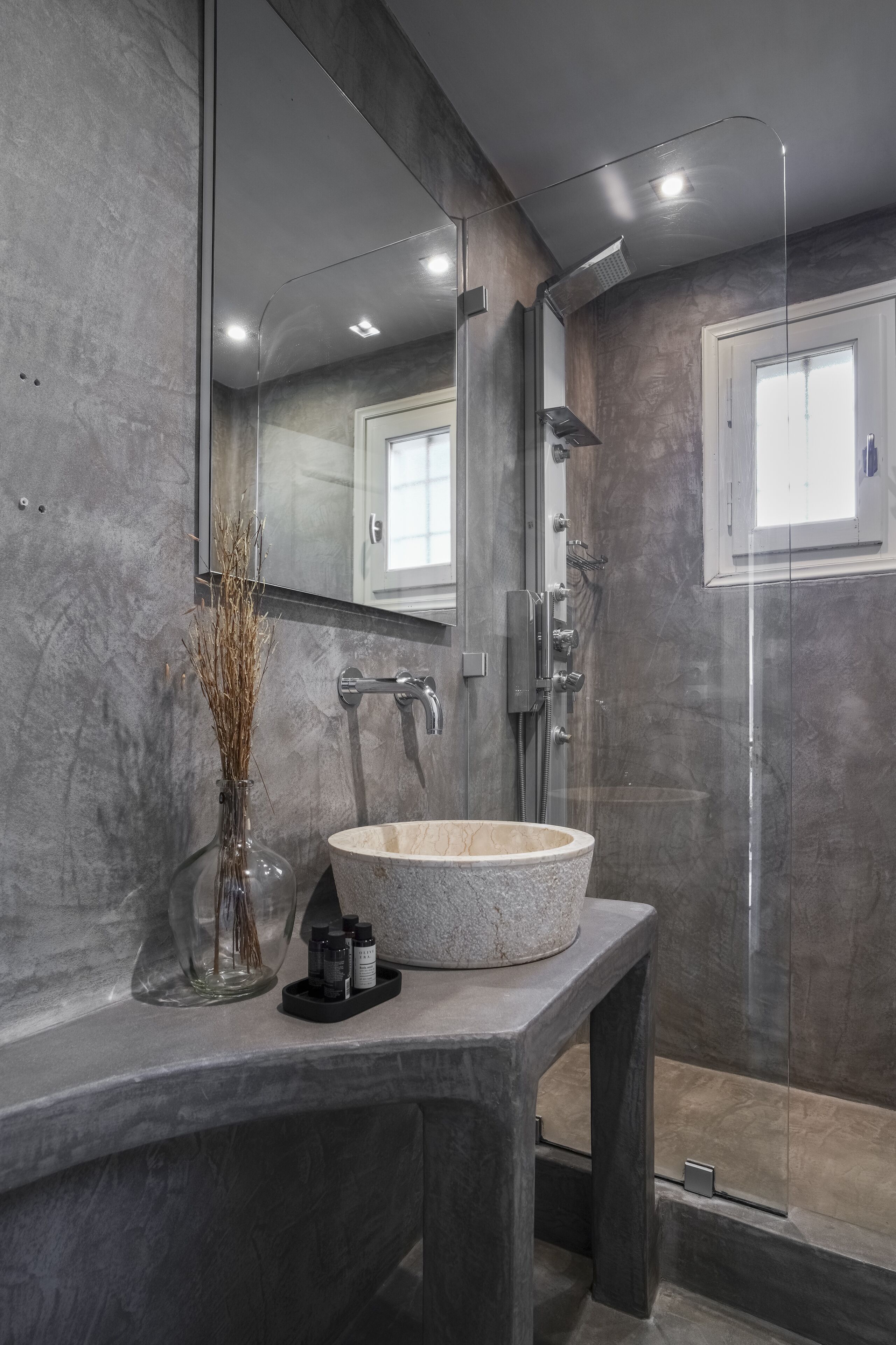 Een moderne badkamer met een grote spiegel, een stenen wastafel en een douche met glazen wanden.