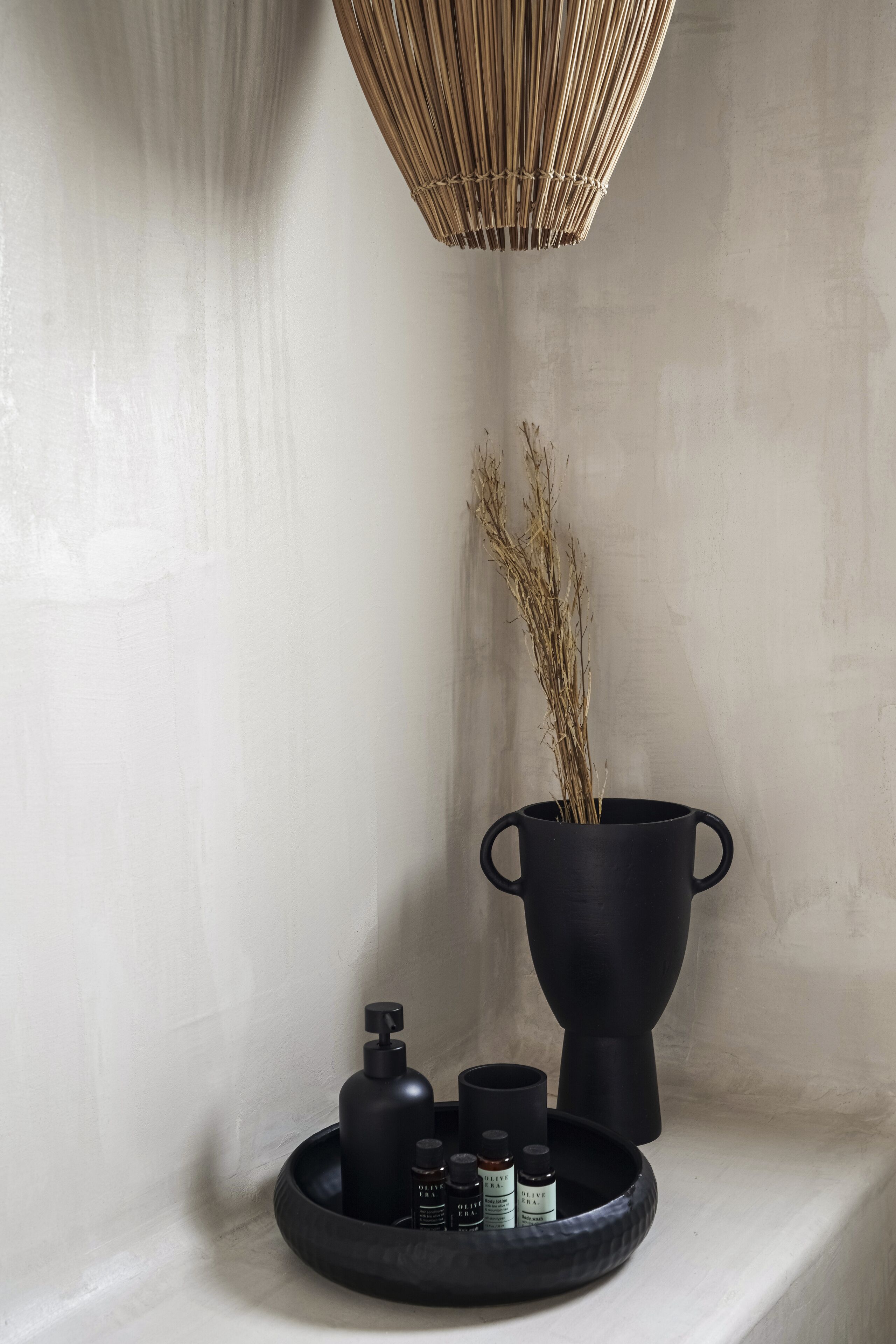 Une salle de bain avec un lavabo noir, un flacon noir et un récipient noir posés sur une étagère.