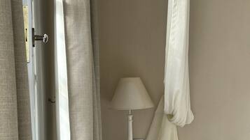 A bedroom with a bed, a nightstand with a lamp, a radiator, and curtains.