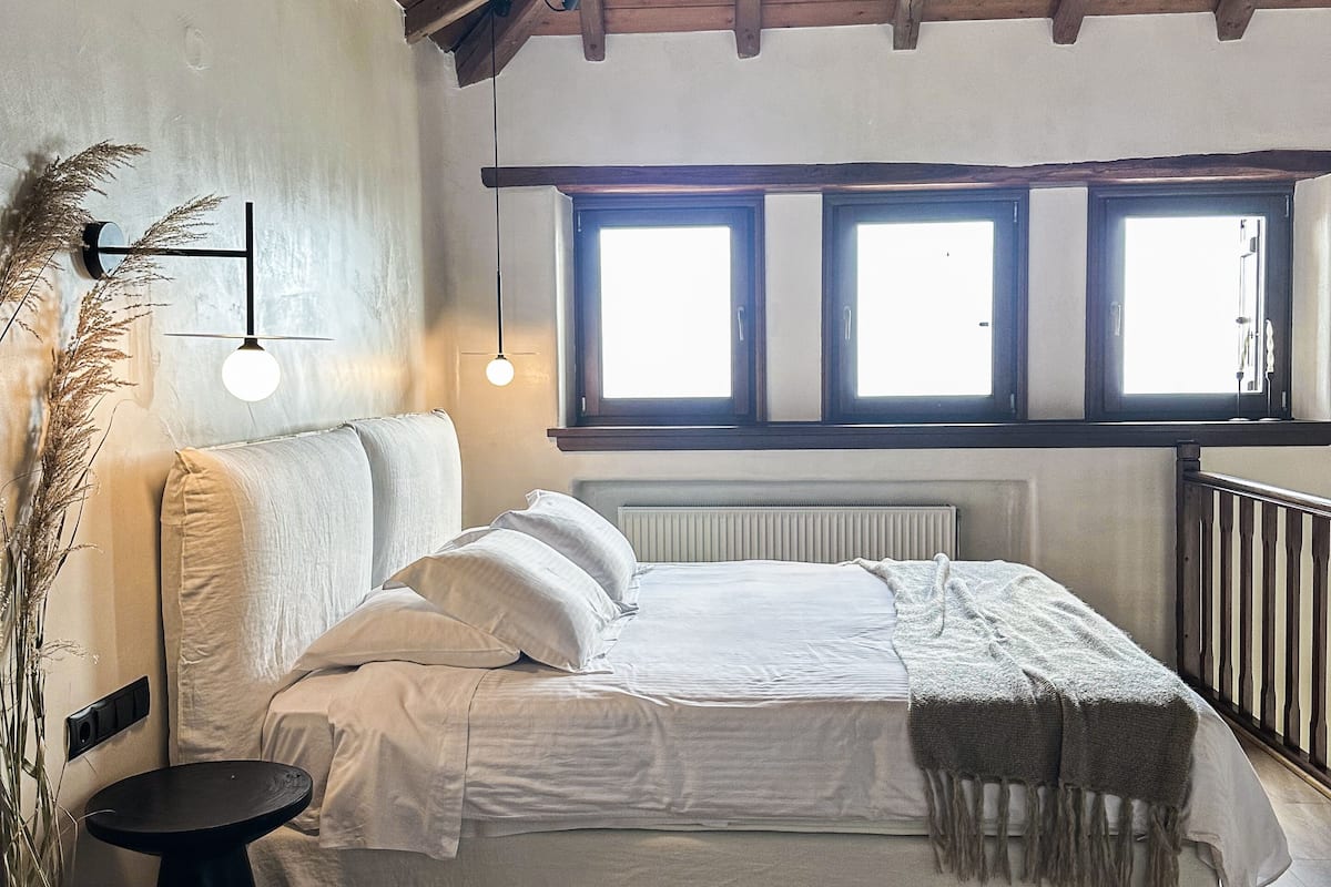 Ein Schlafzimmer mit Holzboden, einem Bett mit weißer Bettwäsche, einem runden Tisch und einer Topfpflanze.