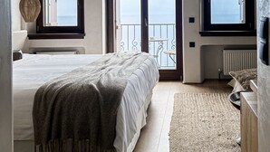 A bedroom with a large bed, a view of the sea through a sliding door, and a balcony with a chair. - Agapitos Villas & Guesthouses (Zagora-Mouresi)