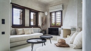 A modern living room with a sofa, two round tables, a television, and a fireplace. - Agapitos Villas & Guesthouses (Zagora-Mouresi)