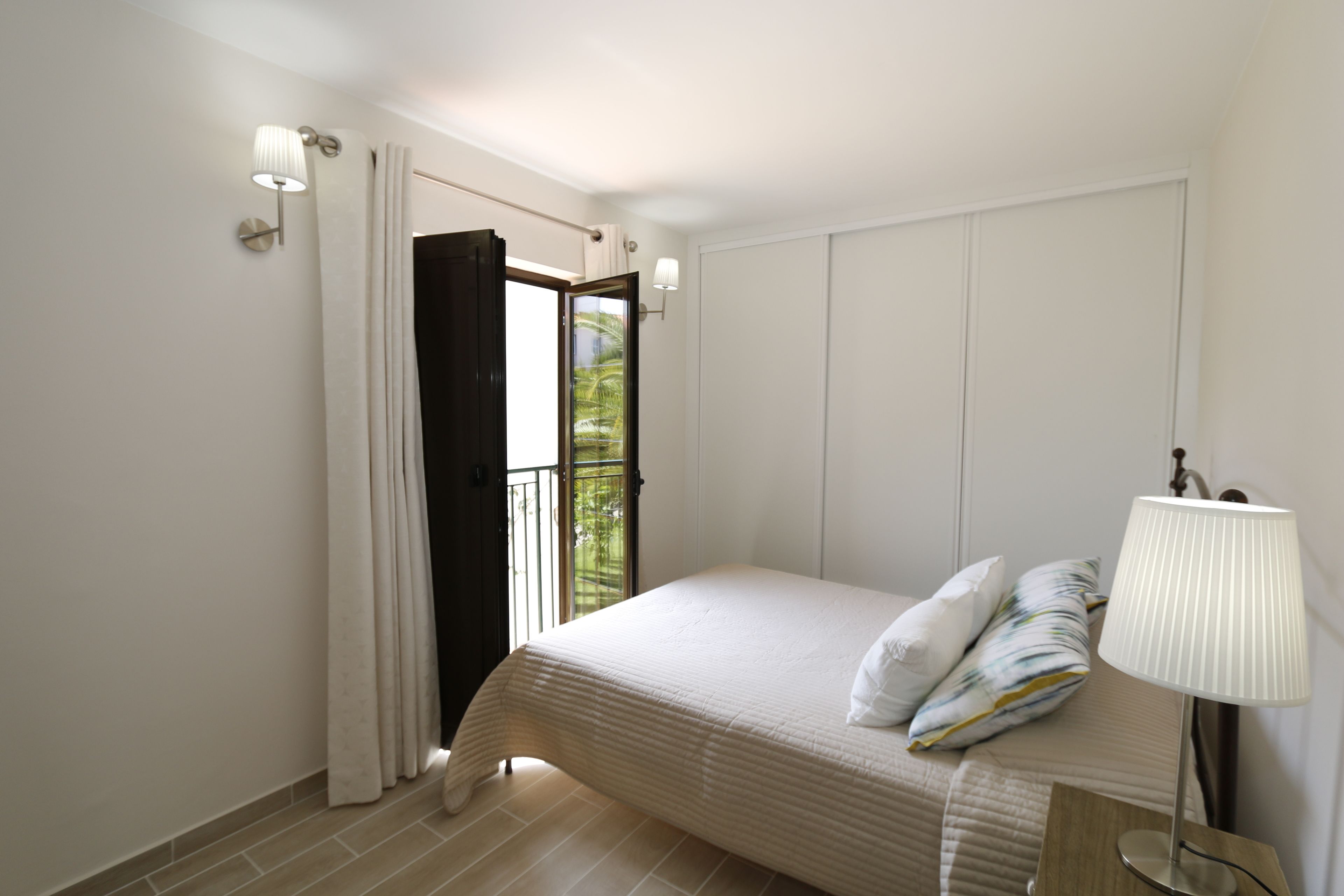Une chambre à coucher avec un lit, une table de chevet, une lampe et une fenêtre avec des rideaux.