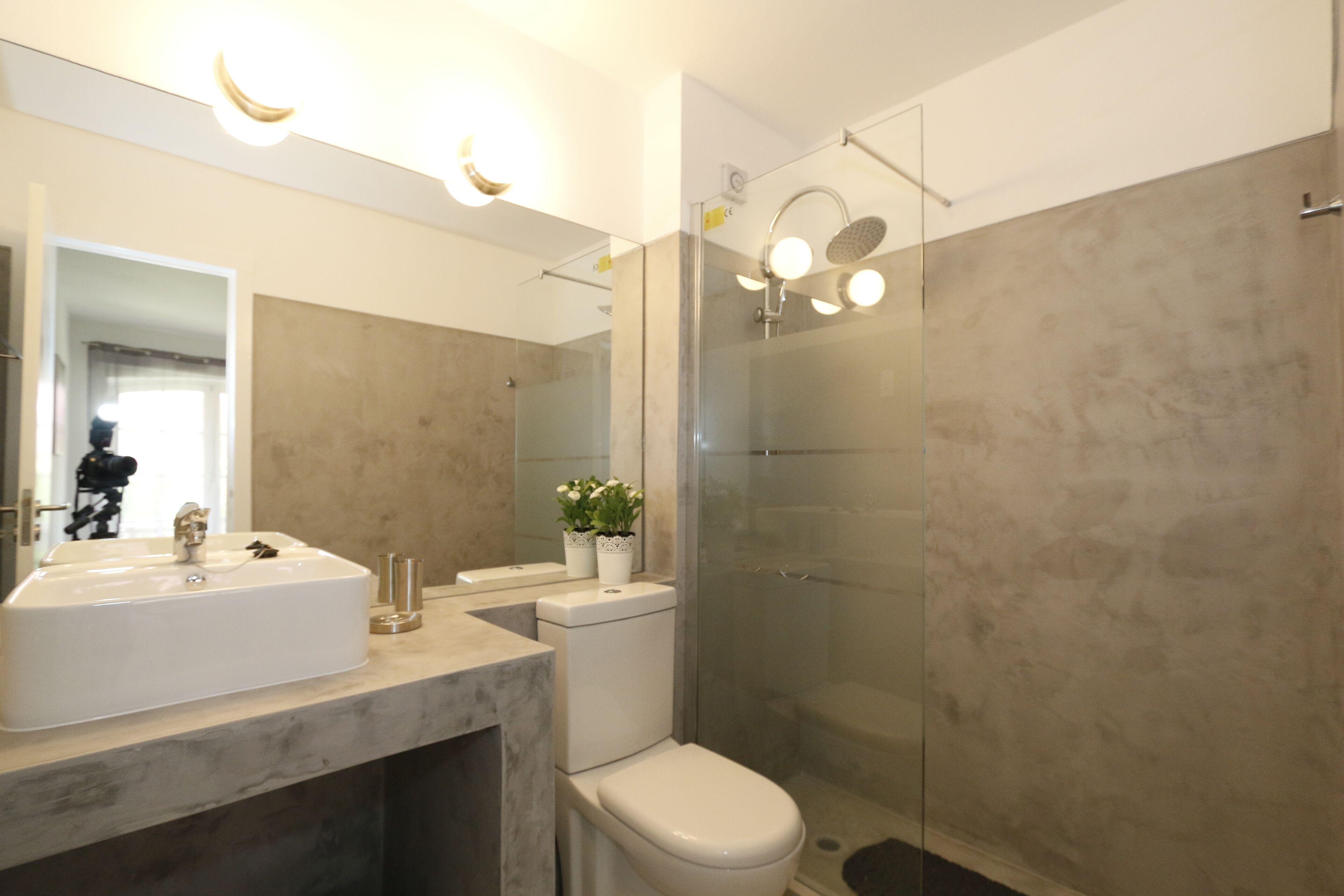 A modern bathroom with a large mirror, a sink, a toilet, and a glass-enclosed shower.