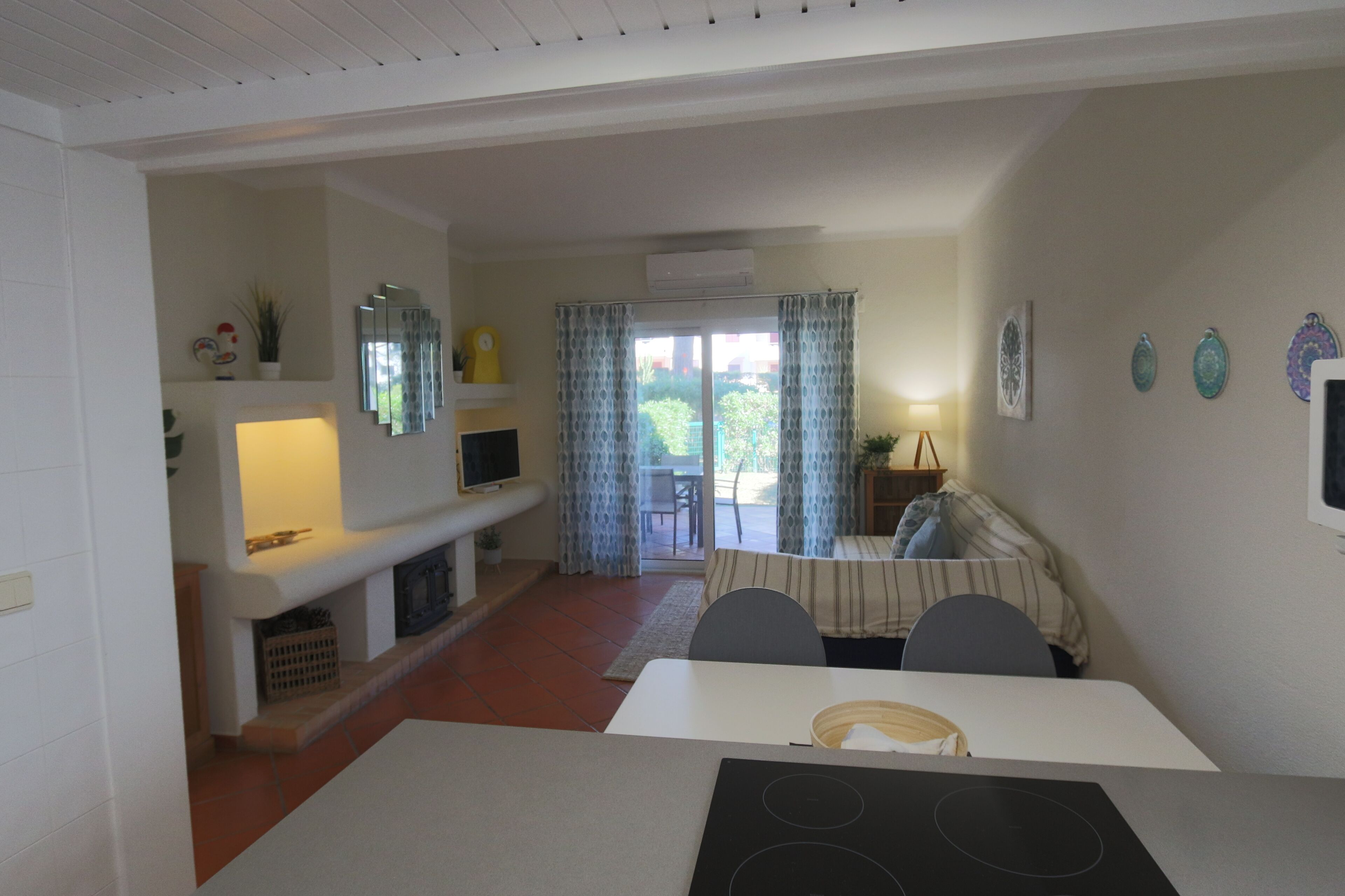A dining area with a table, chairs, and a built-in stove. There is a television on a shelf, a plant, and a window with curtains.
