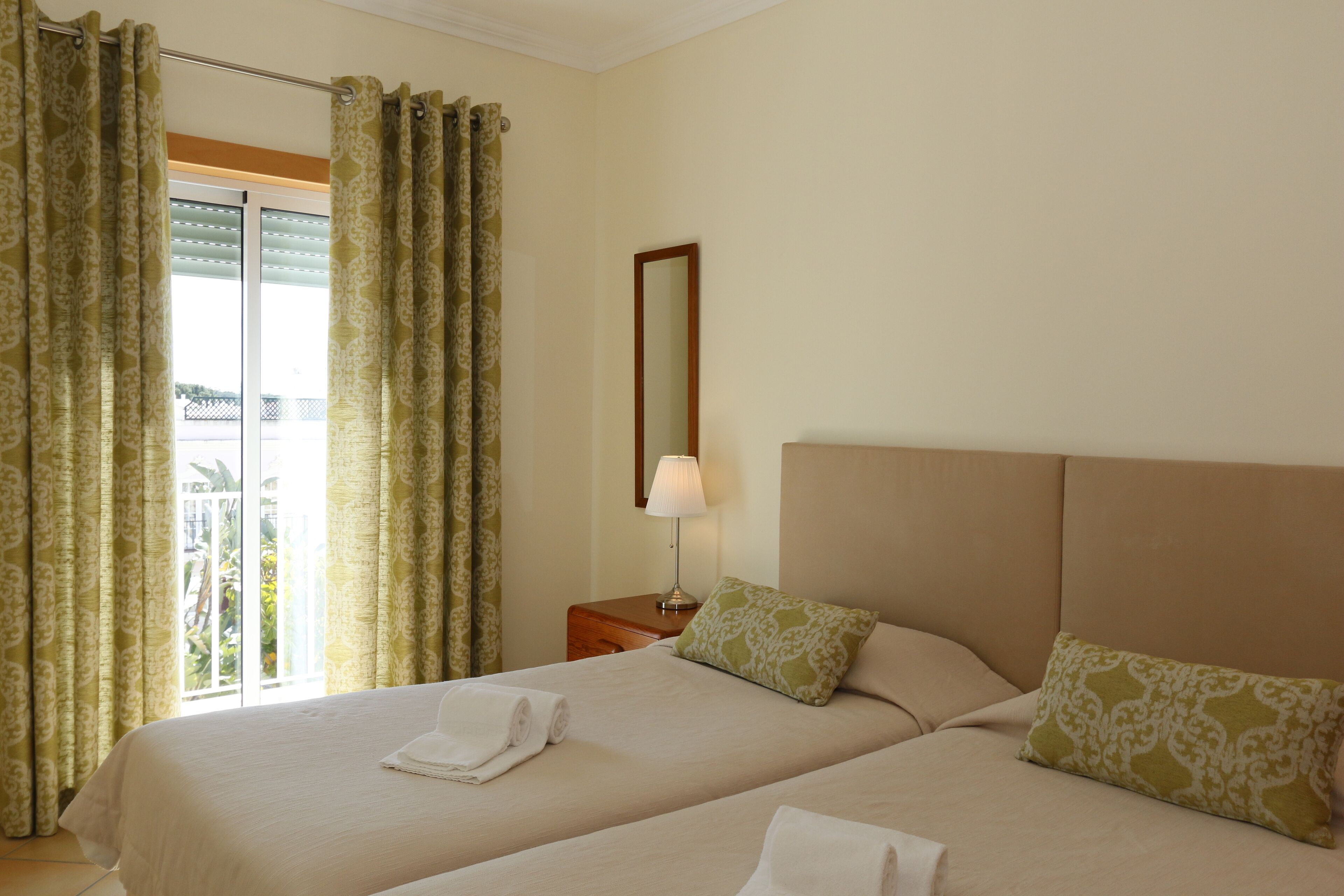 Une chambre d’hôtel avec deux lits, une table de chevet avec une lampe et une vue sur l’extérieur par une fenêtre munie de rideaux.