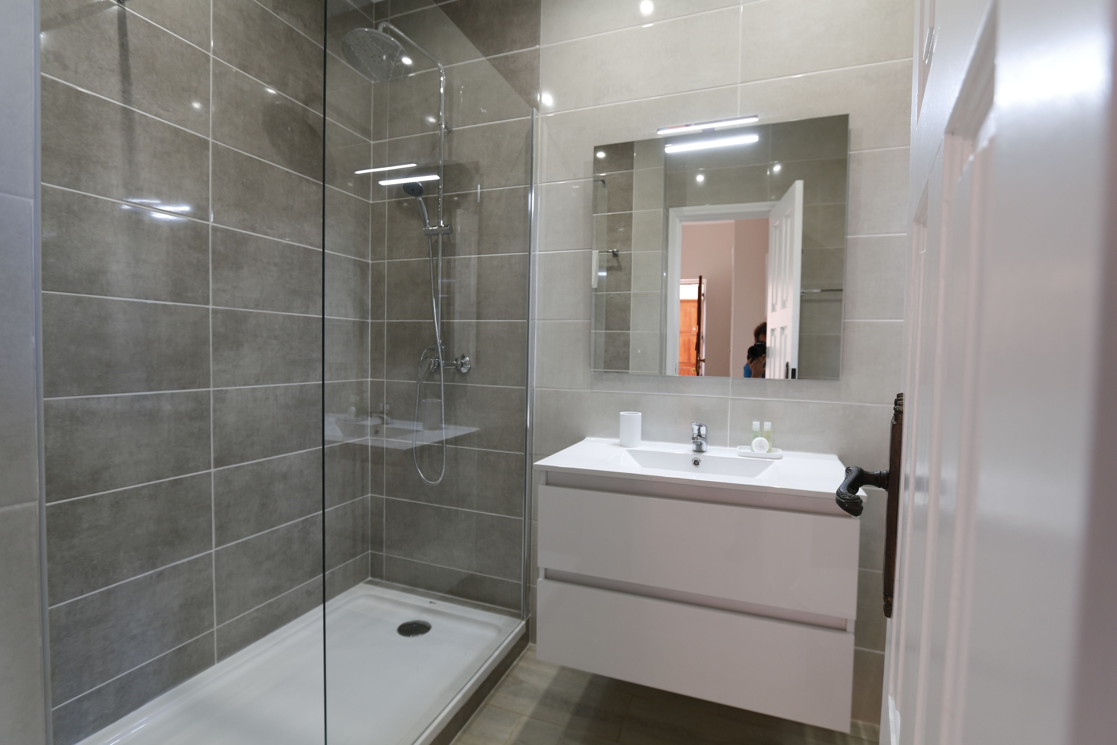 A modern bathroom with a glass-enclosed shower, a white sink, and a large mirror.