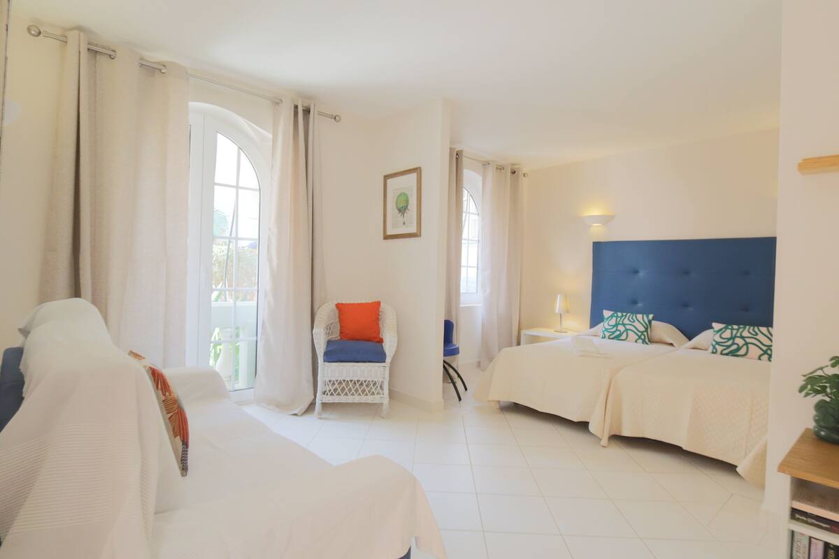 Habitación de hotel con cama, una silla, mesita de noche y ventana con cortinas.