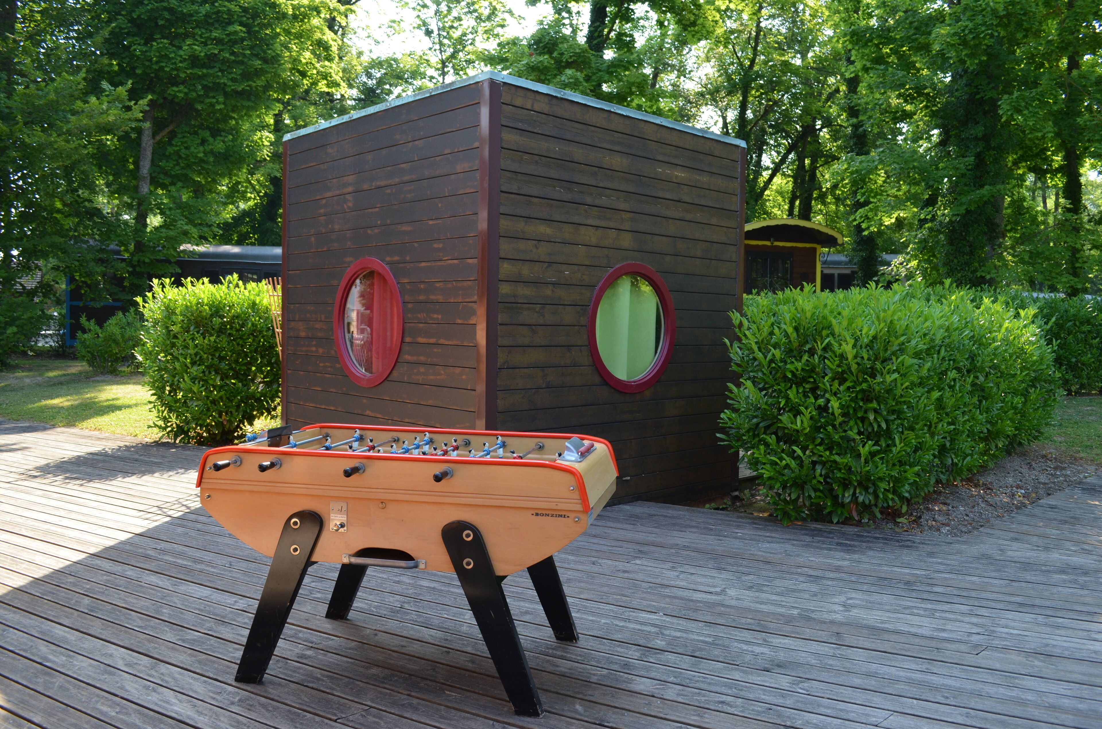 A wooden playhouse with two circular windows and a foosball table in front.